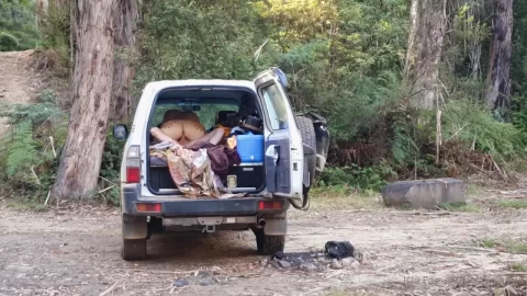 Blonde Woman Kneeling in SUV Cargo Space in Forest Clearing