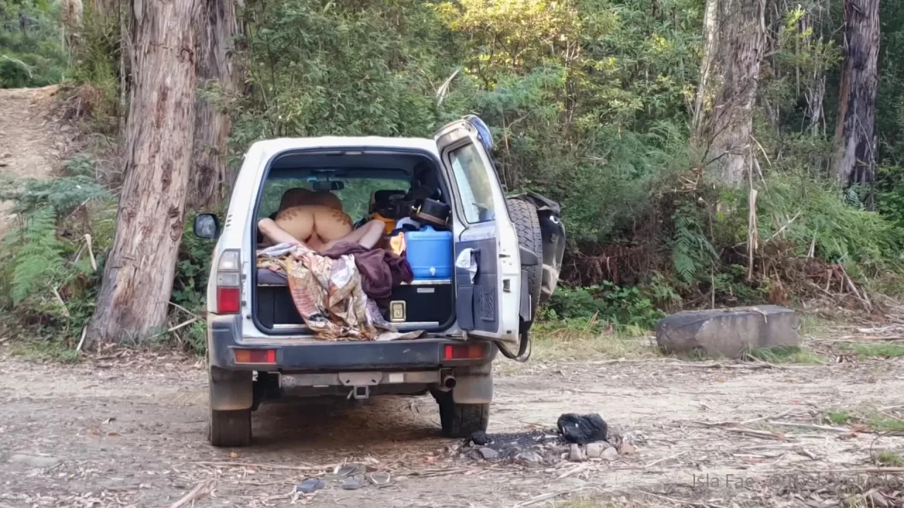 Blonde Woman Kneeling in SUV Cargo Space in Forest Clearing