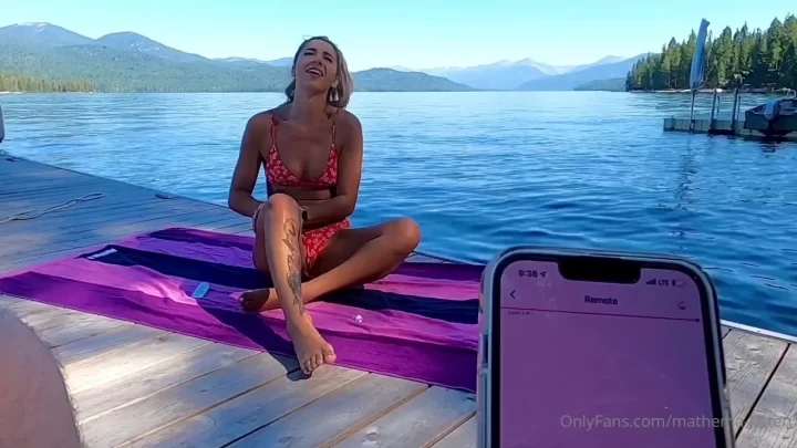 Blonde on a yoga mat by the lake, laughing and stretching in sunlight