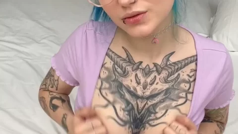 Tattooed blonde girl poses on bed, adjusts shirt