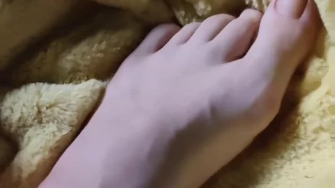 Slim 20s girl plays with her feet on a yellow blanket