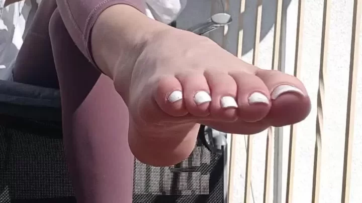 Blonde girl smoking and adjusting sandal on balcony