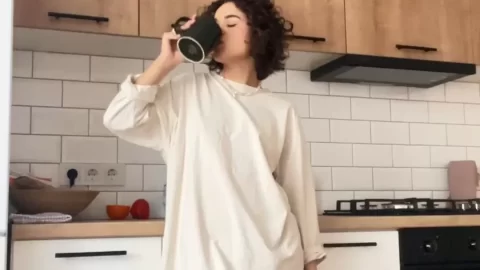 Slim brunette girl drinks from mug in kitchen