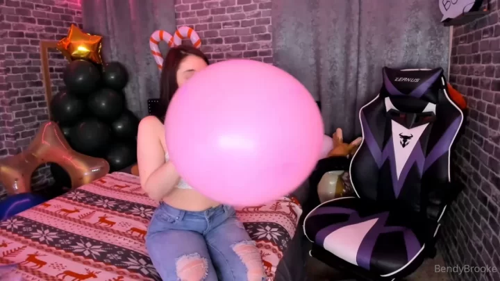 Teen brunette plays with pink balloon on bed