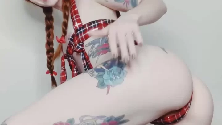 Redheaded girl kneels on black blanket, exposes butt